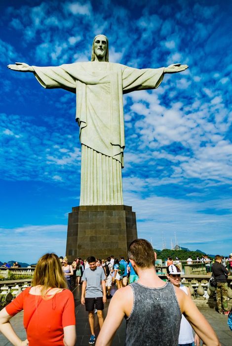 Casal de turistas posando para foto no Cristo Redentor. Visite o Rio de Janeiro com a Agência 7 Quedas e viva a sua melhor experiência de viagem. @7quedasviagensrj